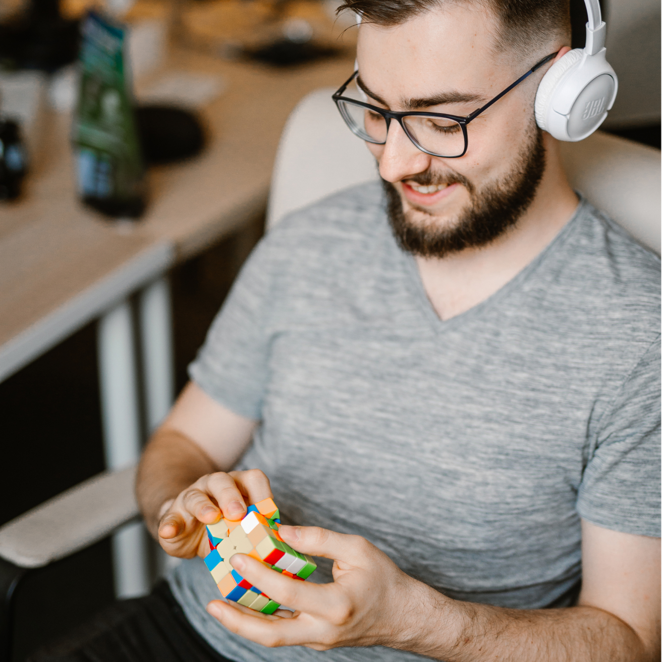 A developer playing a Rubik's cube. He's wearing glasses, white headphones and gray T-shirt