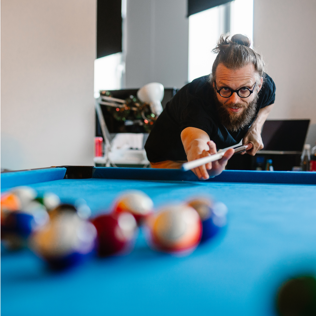 A developer with a beard and glasses is engaged in a game of pool, concentrating on his next move at the table.