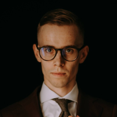Portrait of a man in a suit and glasses, looking composed against a neutral background.