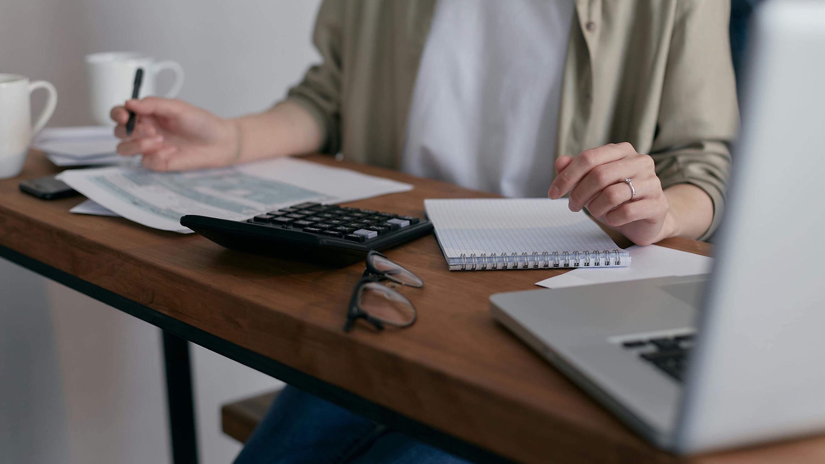 Person at desk working with calculator, laptop, and financial papers