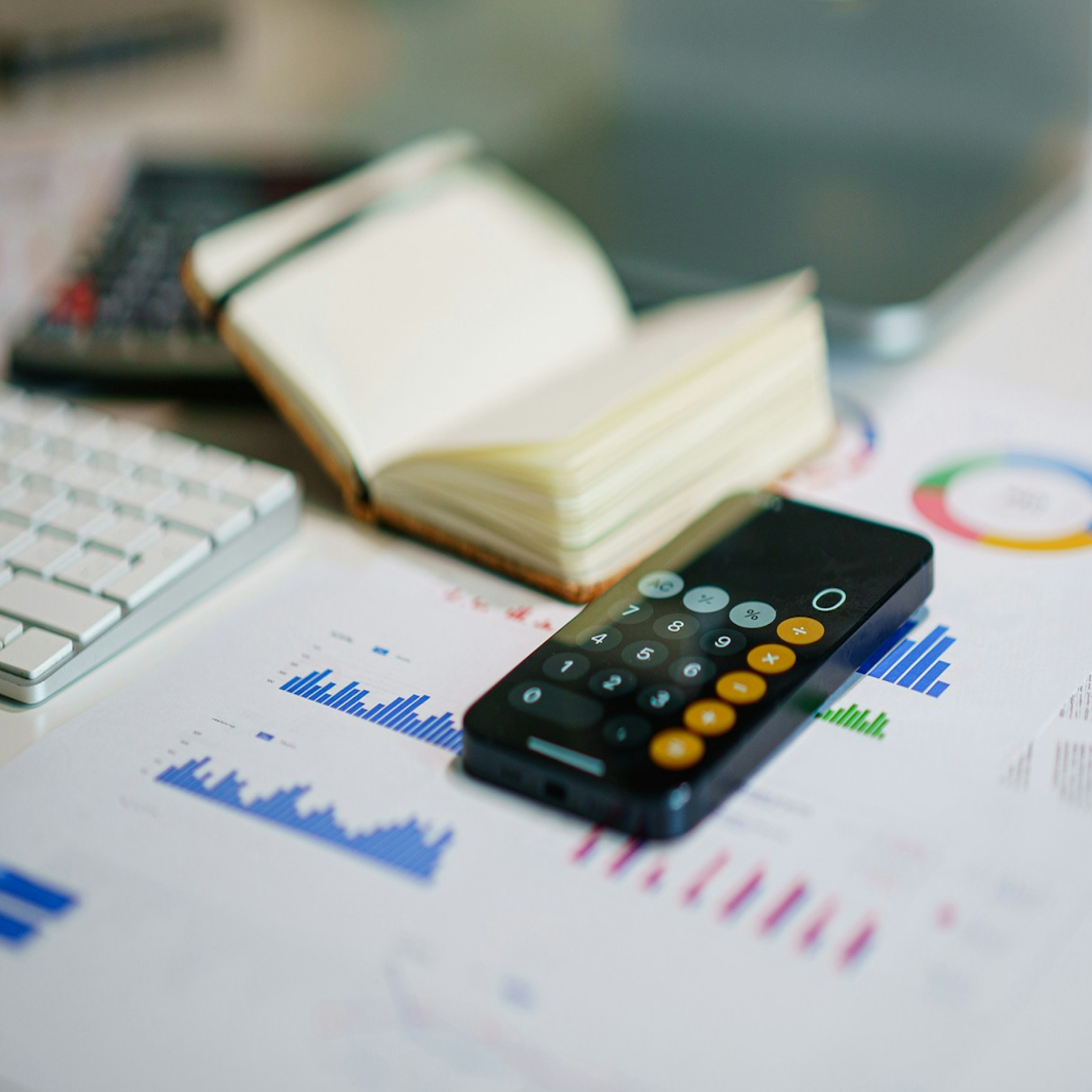 A smartphone lying on documents with graphs, next to a notebook and keyboard, representing financial data and personal loans.