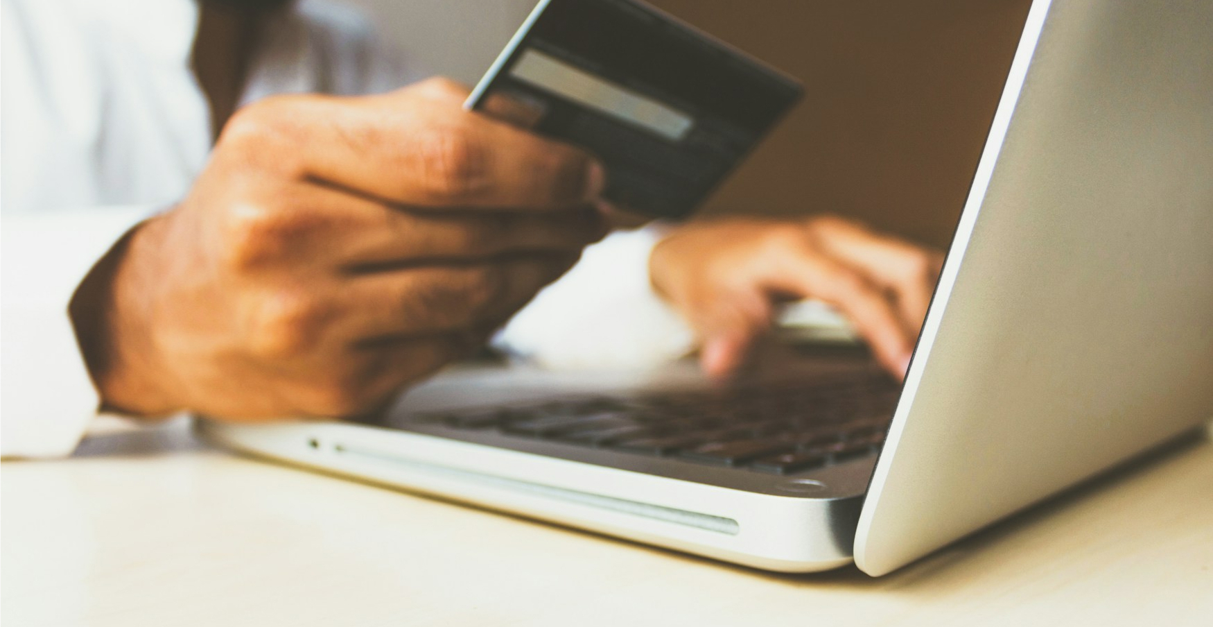 Person holding a credit card while using a laptop, suggesting an online payment or e-commerce transaction.