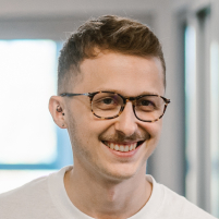 A man standing in the office and smiling, wearing glasses and a white shirt