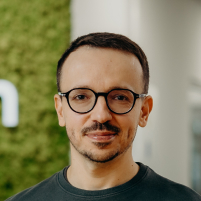 A man standing in the office and smiling, wearing glasses and a green shirt,