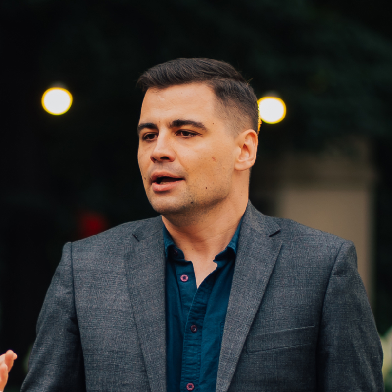 A man dressed in a gray suit, exuding professionalism and elegance, stands confidently with a neutral background.