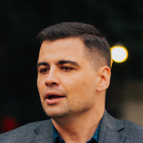 A man dressed in a gray suit, exuding professionalism and elegance, stands confidently with a neutral background.